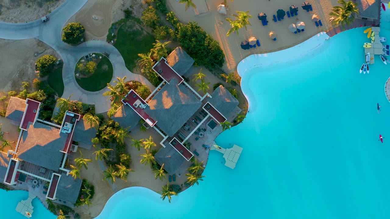 Top-down view at Diamante Cabo San Lucas with turquoise pool water, clustered resort roofs, palm landscaping, sandy paths, and no visible people.