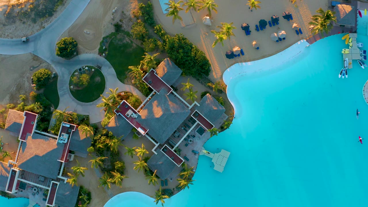 Pool, villas, palm trees, circular garden, and curved roadway from above.