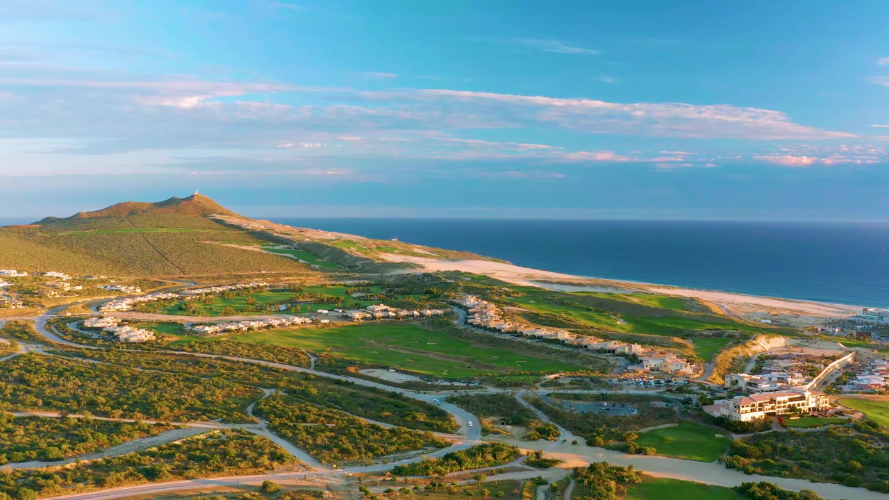 Drone view of a coastal hill and beach with roads and green areas.