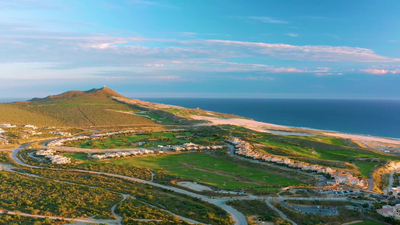 Wide aerial of hillside roads and buildings beside a sandy beach and ocean.