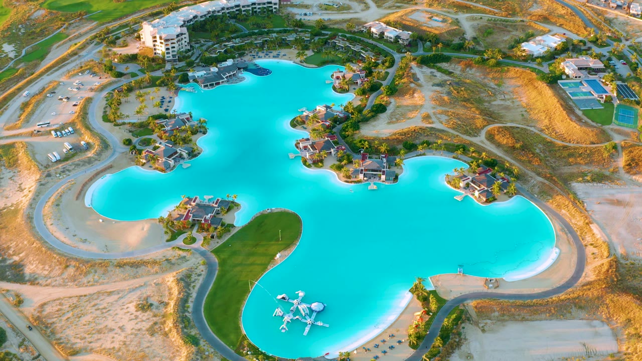 Drone view of a bright blue lagoon with roads, villas, and dry construction terrain.