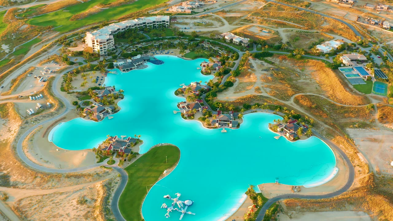 Aerial lagoon scene with turquoise water, roads, sandy lots, buildings, and green patches.