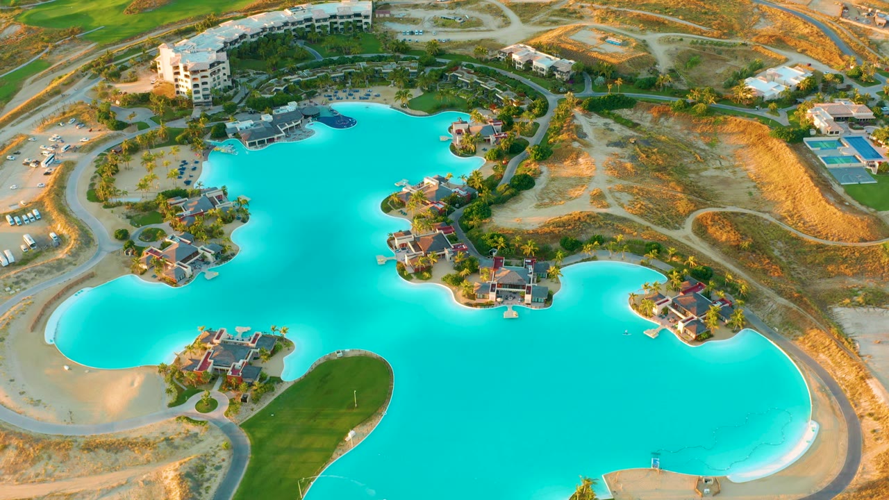 Drone view of a blue lake beside dry development land and residential islands.