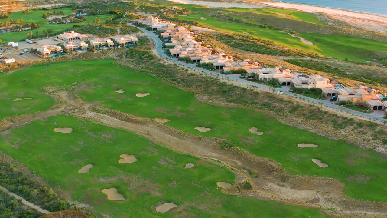 Golf course fairways and sand traps below a row of coastal homes.