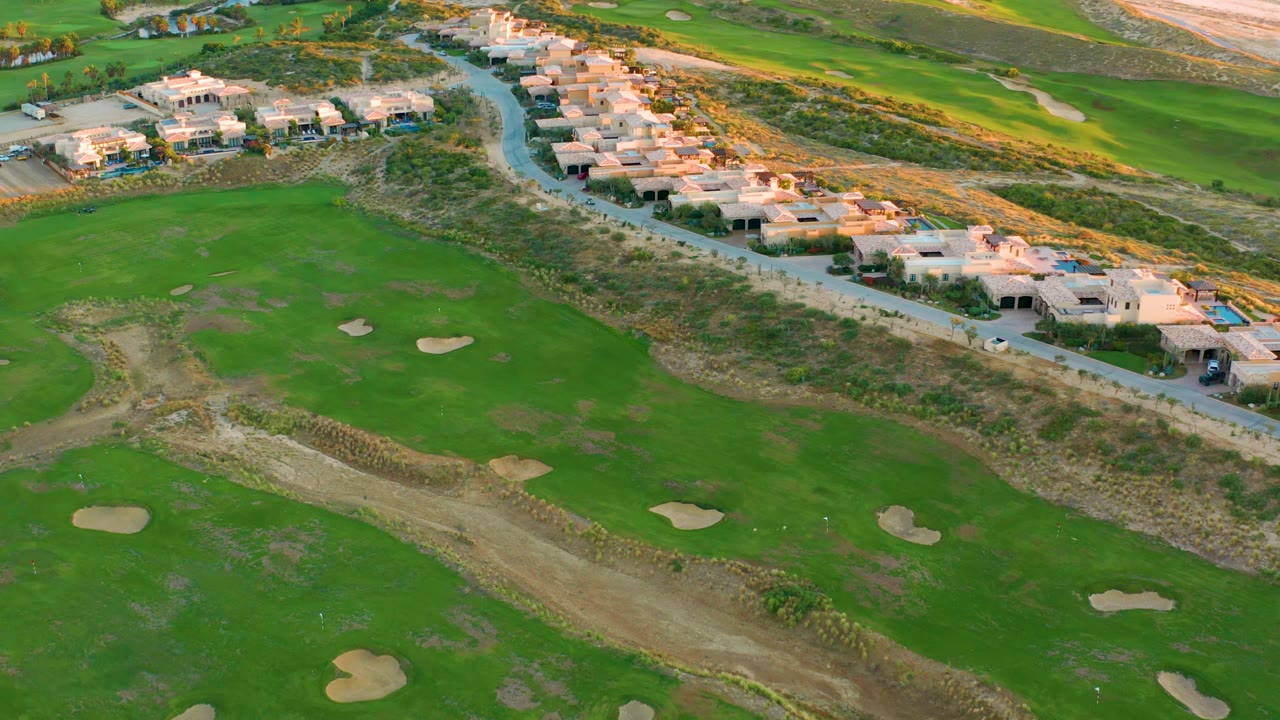Golf course fairways and sand traps below a row of coastal houses.