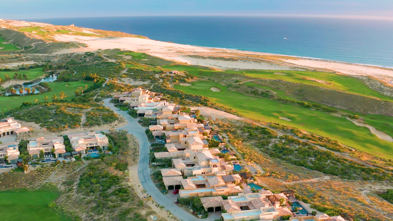 Homes and road below a coastal golf course with beach and ocean beyond.
