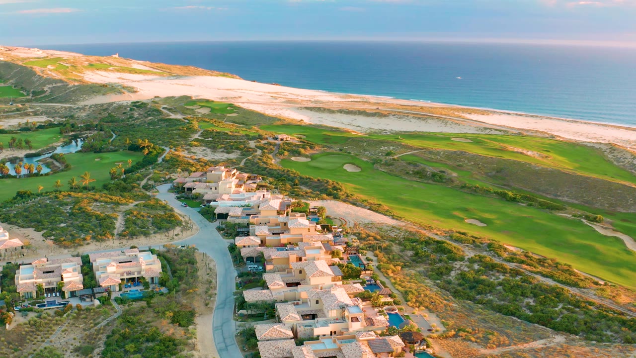 One second into the clip, the Diamante Cabo San Lucas aerial holds the homes lower in frame with fairways, bunkers, dunes, beach, ocean horizon, and no visible people.