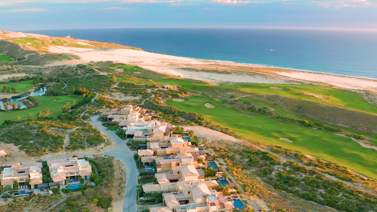 Aerial coastline with homes, fairways, dunes, beach, and ocean.