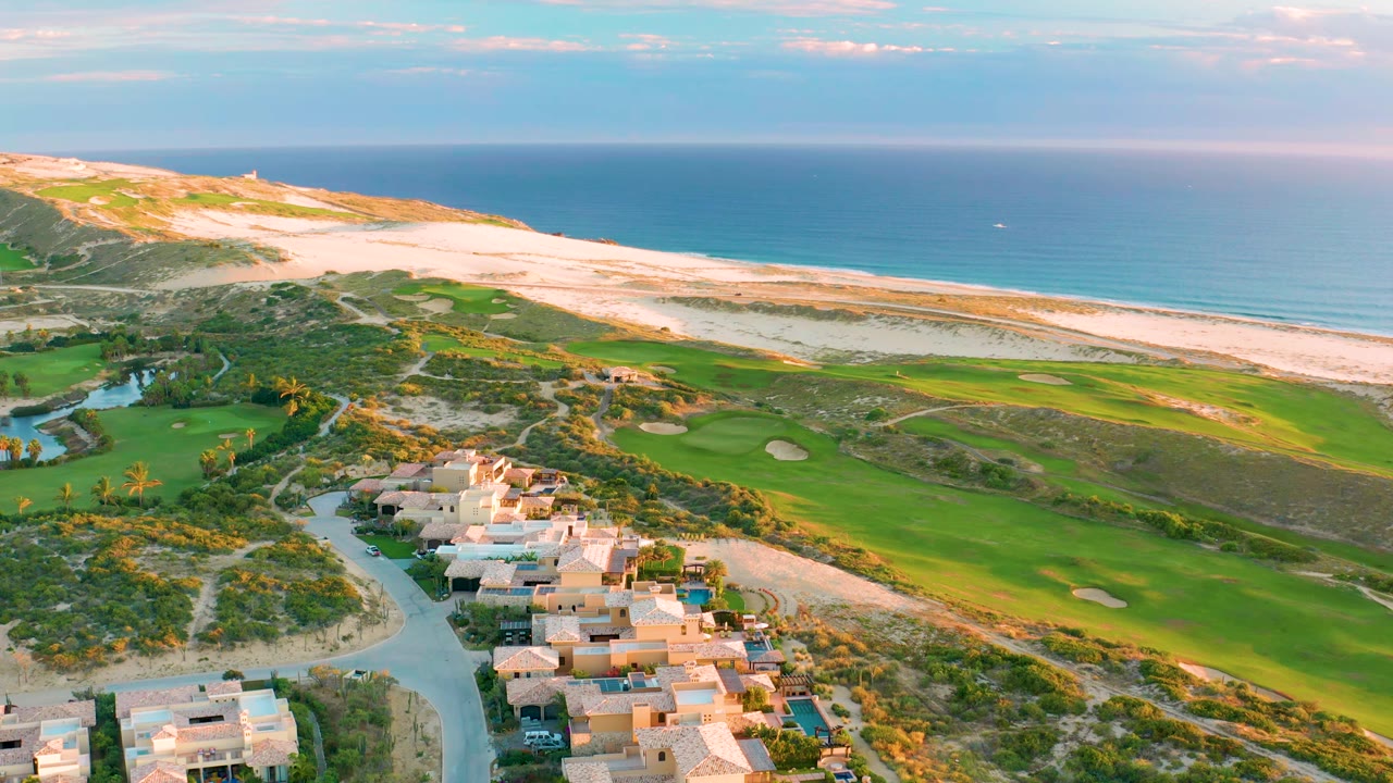 Wide drone view of golf fairways beside dunes and ocean.