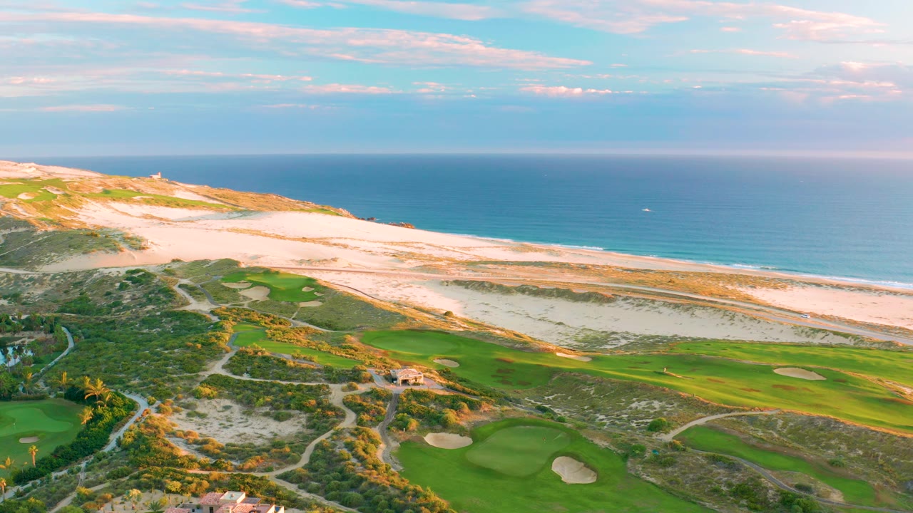 Wide aerial of dunes and ocean above coastal golf greens.