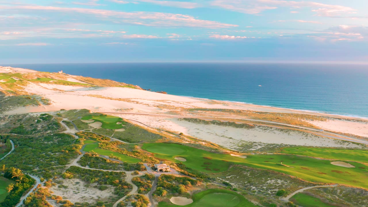 Coastal golf course with fairways, bunkers, sandy beach, and ocean horizon.