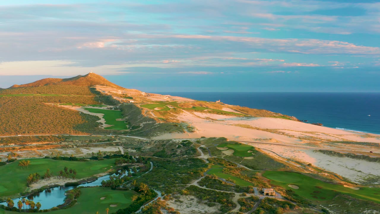 Aerial coastal scene with dunes, pond, green fields, hill, and ocean horizon.