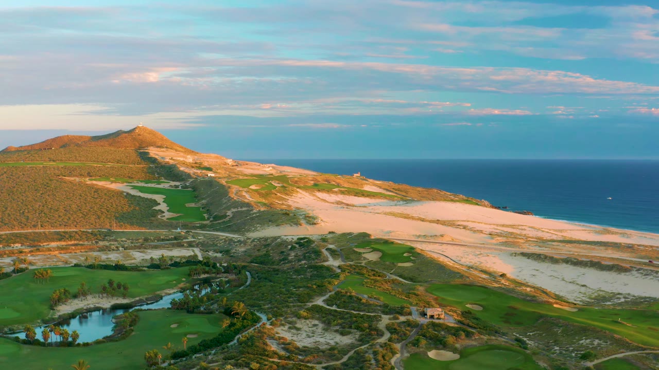 Coastal golf course beside dunes and ocean with a small house near the lower edge