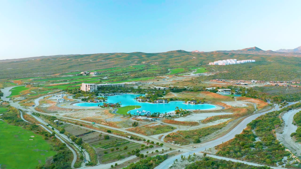 Aerial view of blue reservoir, winding roads, green fields, buildings, and hills.