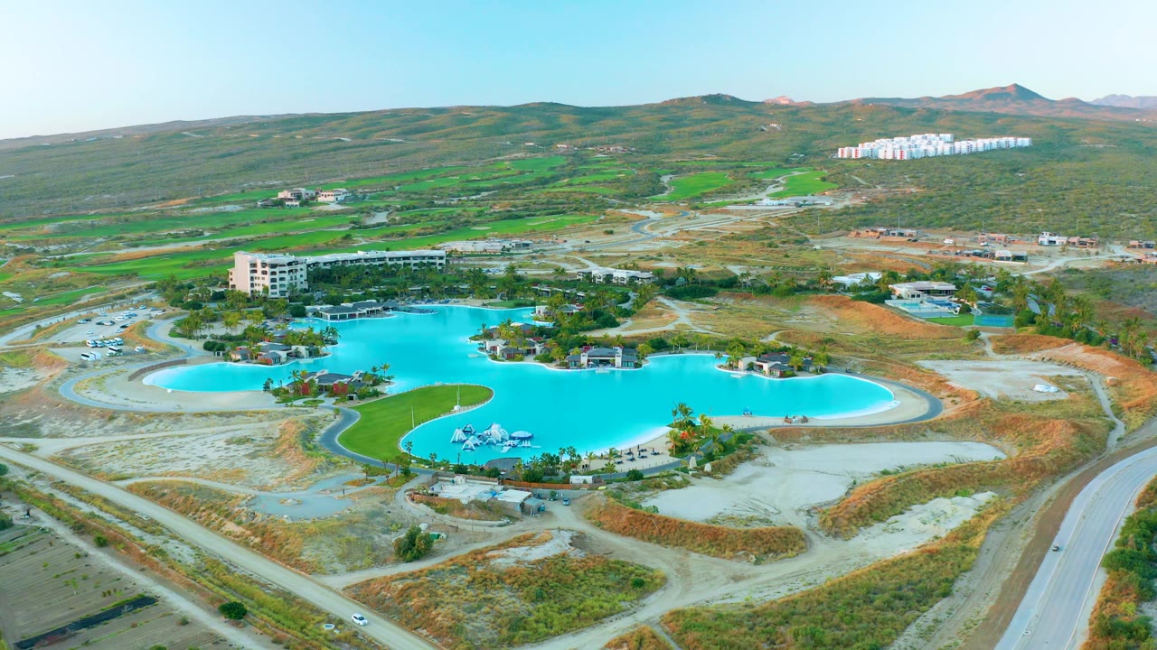 Wide aerial of a pool area with a road in the foreground and hills behind.