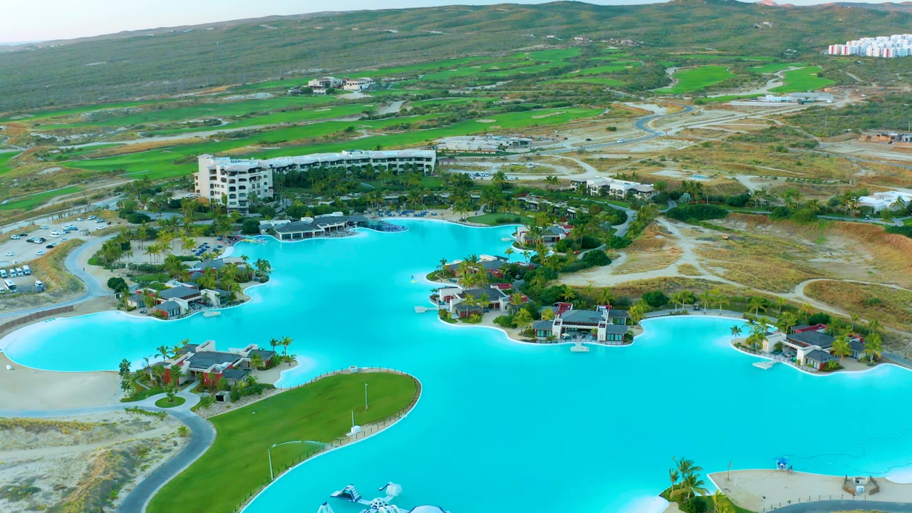 Wide aerial of a resort lagoon with green lawns and hillside roads.