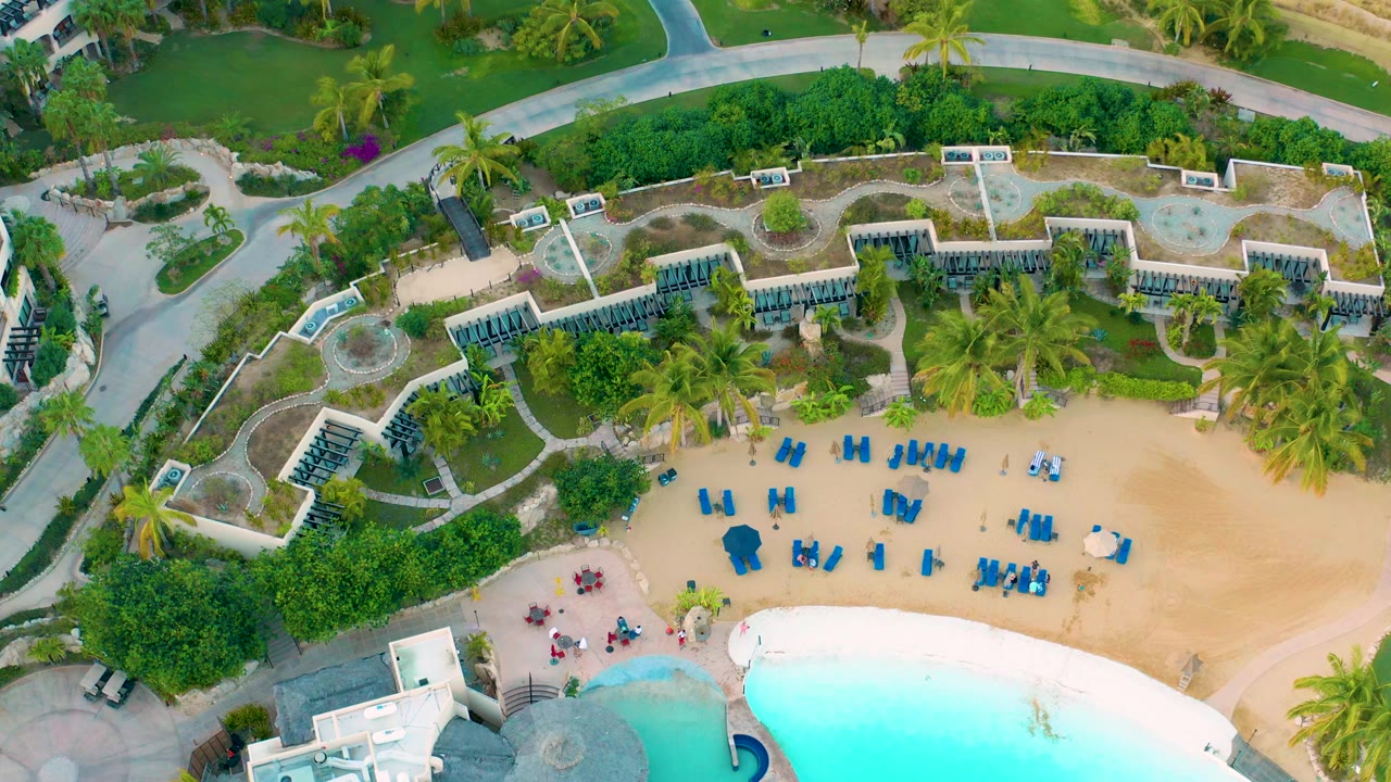 Aerial view of pool edge, sand, lounge chairs, palms, and resort landscaping.
