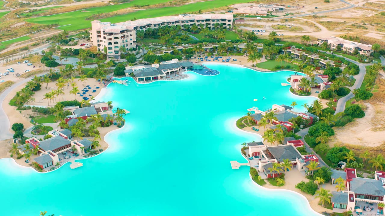 Turquoise lagoon bordered by buildings, palms, roads, and sandy ground.