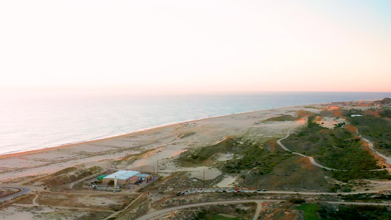 Aerial shoreline view with beach, ocean, dunes, roads, and low vegetation.