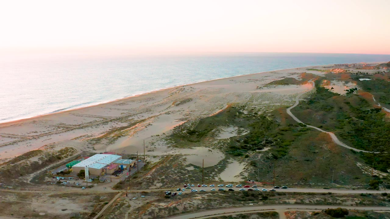 High aerial view of a tarp-covered coastal building below dunes, beach, and ocean.