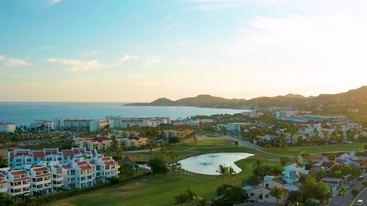 Sunlit coastal residential area with golf course pond and ocean beyond.
