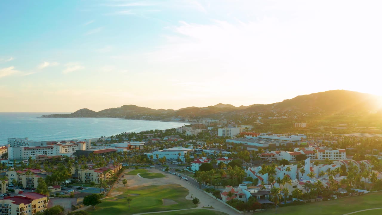 Aerial resort view with golf green, palm trees, ocean, and strong sunset glare
