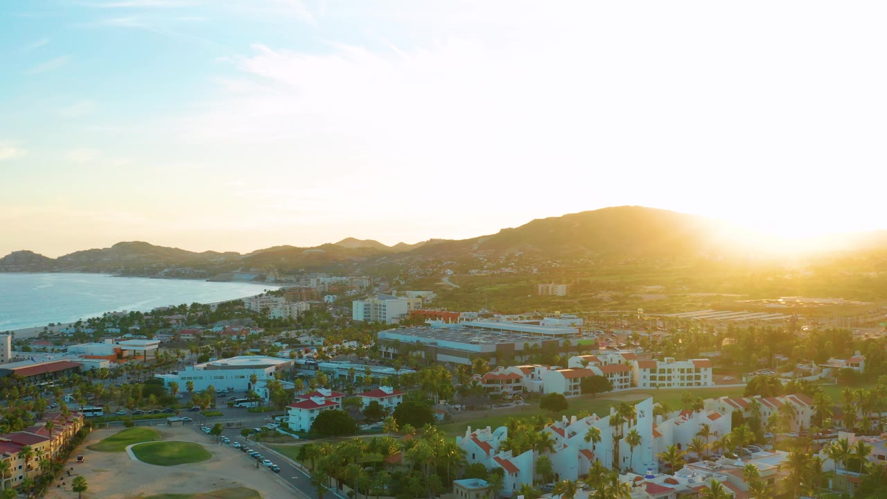 Bright sunset over coastal city with golf course foreground and ocean to the left.