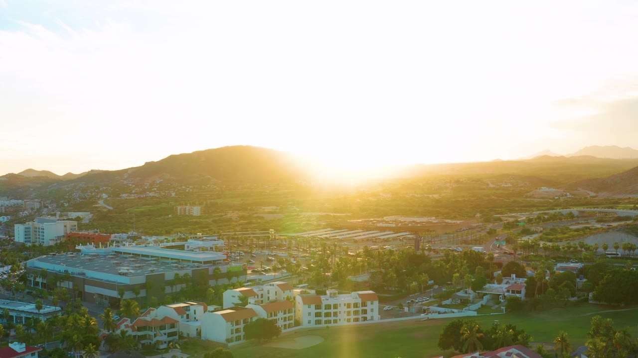 San Jose Del Cabo aerial frame with bright sun flare near the horizon, low mountains behind the city, and no visible people.