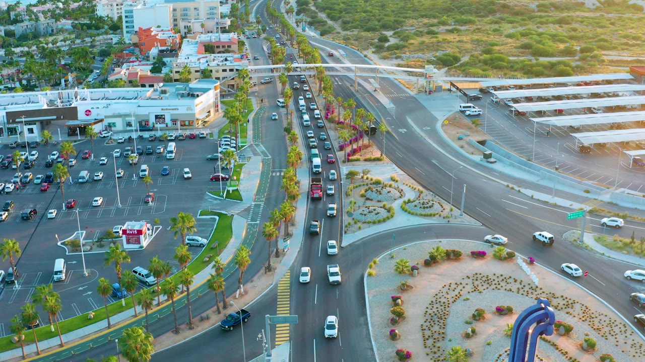 High aerial view of traffic lanes, parked cars, palms, and commercial buildings in daytime light.