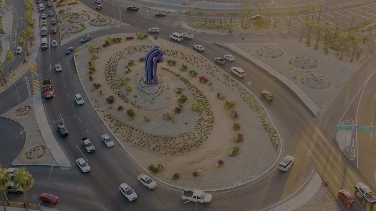 Aerial frame from San Jose Del Cabo showing vehicles entering and circling a landscaped roundabout with a blue central structure and no visible people.