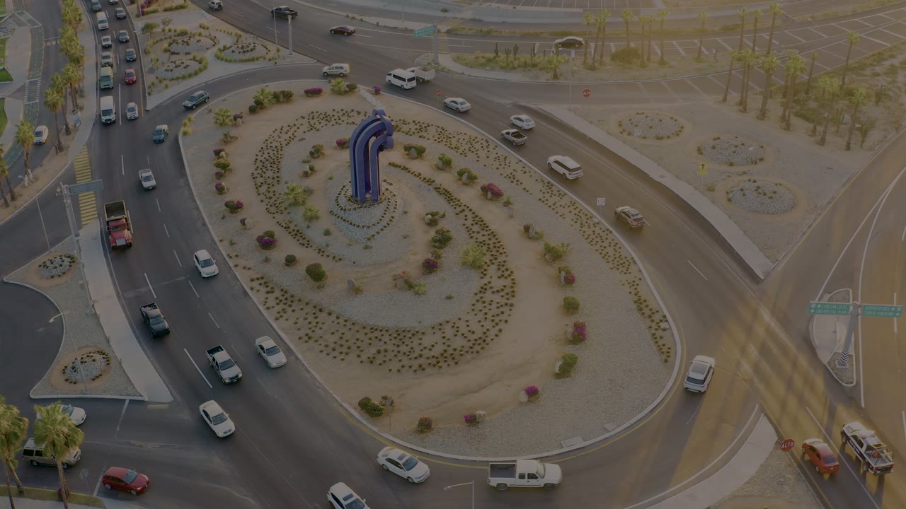 San Jose Del Cabo roundabout seen from above, with cars spaced across the lanes, a pale landscaped center, and no visible people.
