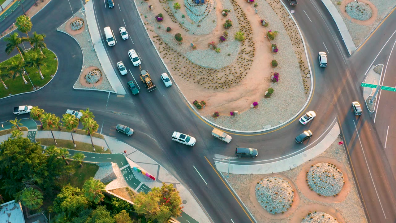 Top-down road junction with cars curving around a planted central island.