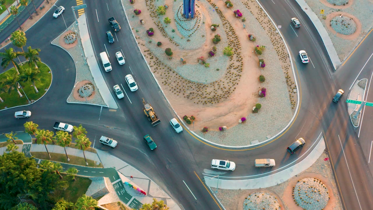 Aerial view in San Jose Del Cabo, Baja California Sur, showing several vehicles entering and circling a landscaped roundabout with desert planting and no visible people.