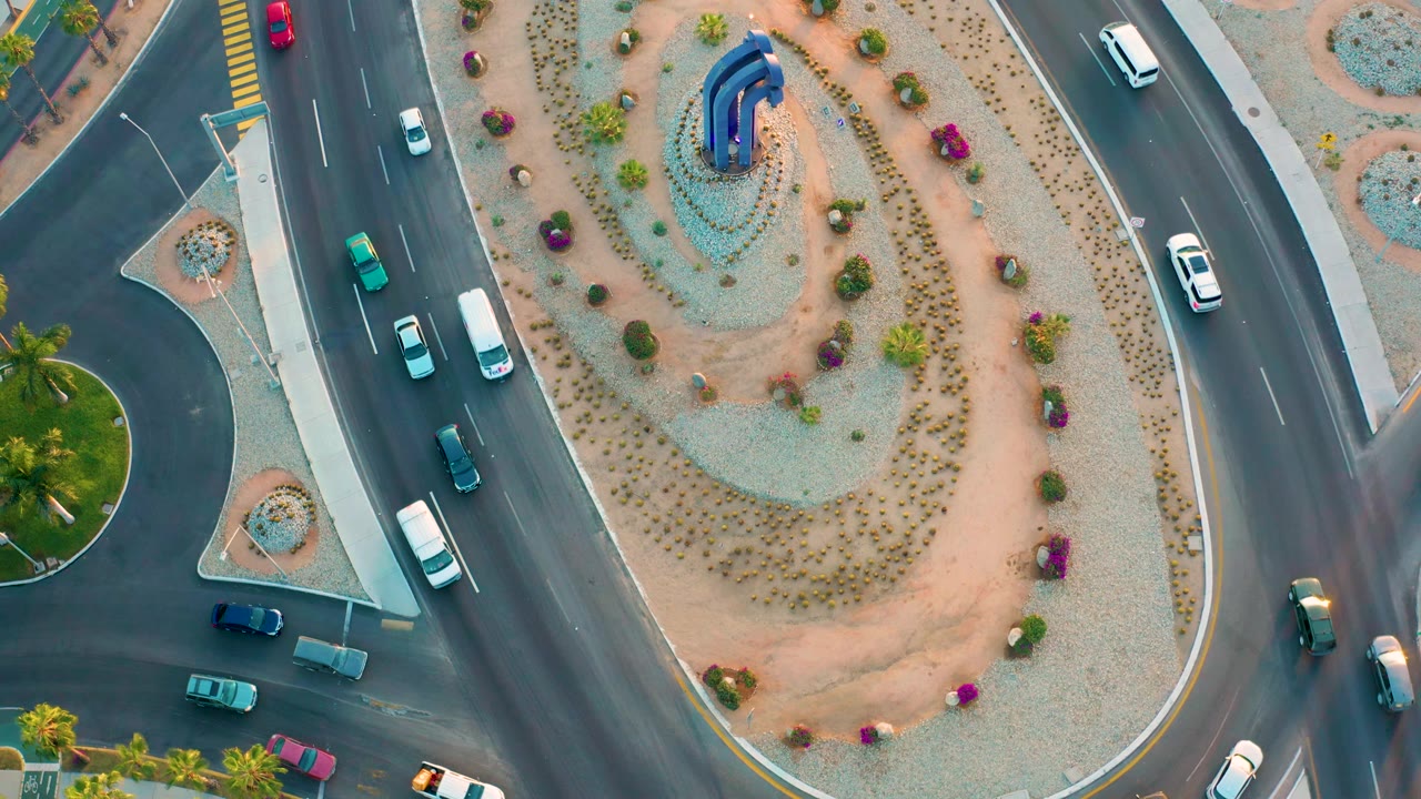 Cars pass a traffic island with desert landscaping