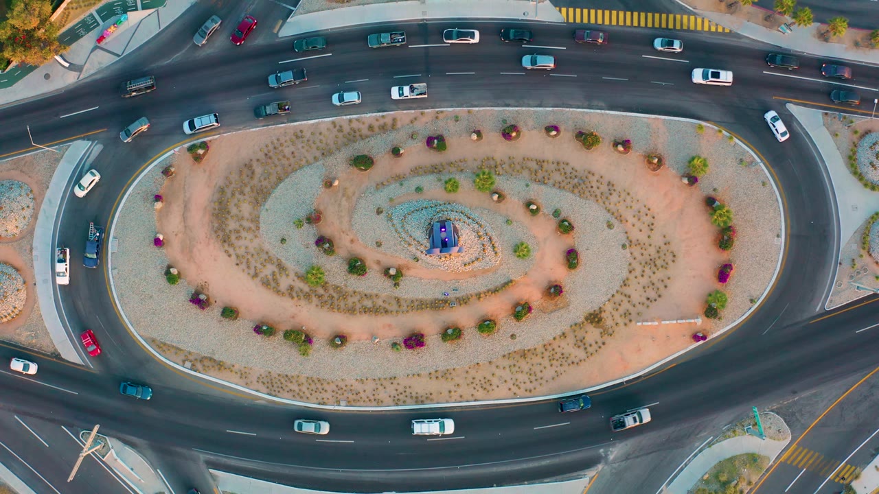 Cars travel along the lower arc of a landscaped traffic circle.