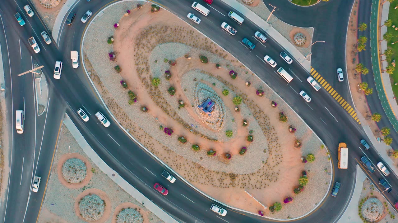 Top-down San Jose Del Cabo road scene with cars circulating and an orange bus or large vehicle entering the right side of the roundabout, with no visible people.