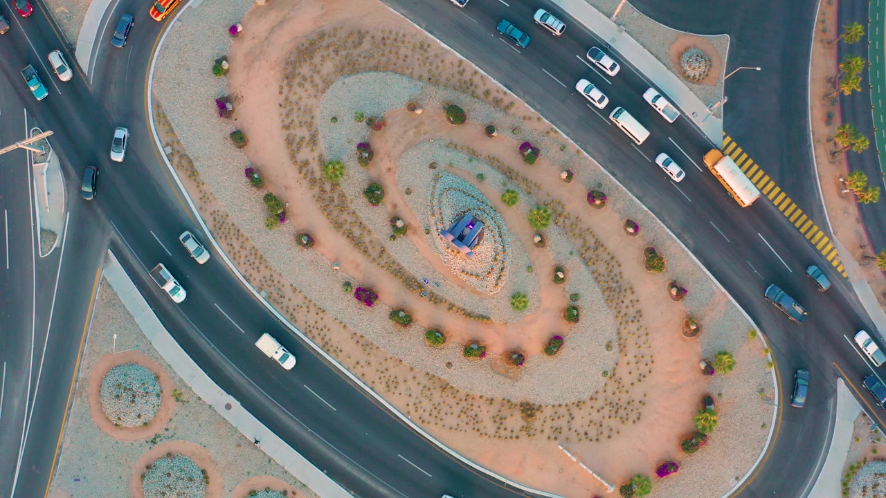 Overhead drone view of vehicles moving around a landscaped roundabout in San Jose Del Cabo, Baja California Sur, with no visible people.