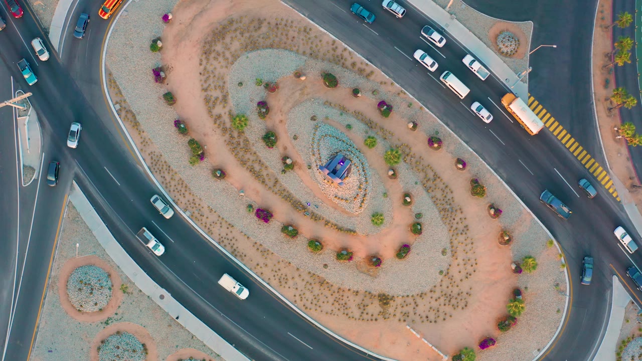 The overhead frame keeps the landscaped island centered while cars and a yellow bus circulate on the bordering roads in San Jose Del Cabo, with no visible people.