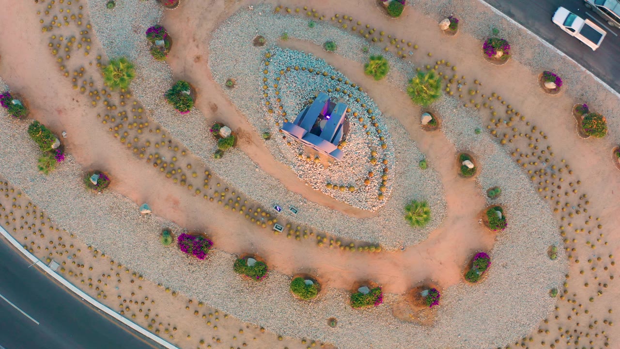 Overhead spiral garden with central monument and a white car near the road.