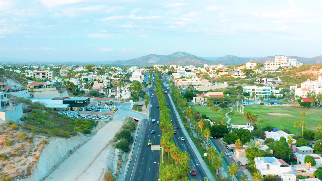 Aerial view of a multi-lane road beside a dry riverbed and green field.