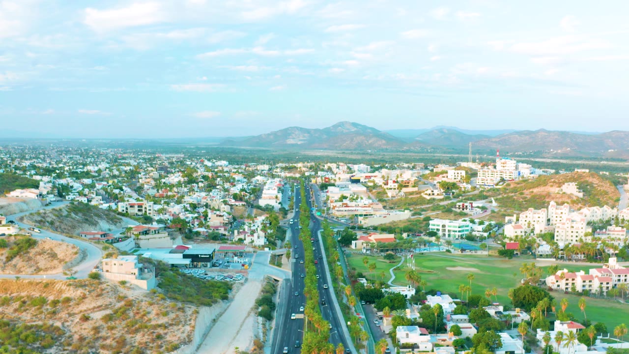 Aerial cityscape with a central road and distant hills under clouds