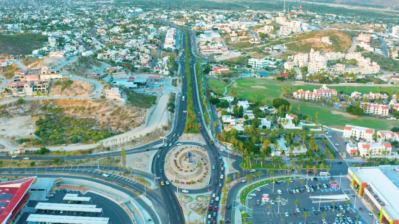 Third frame shows the San Jose del Cabo road corridor continuing toward the horizon, with the roundabout below, scattered vehicles, white buildings, construction ground, and no visible people.