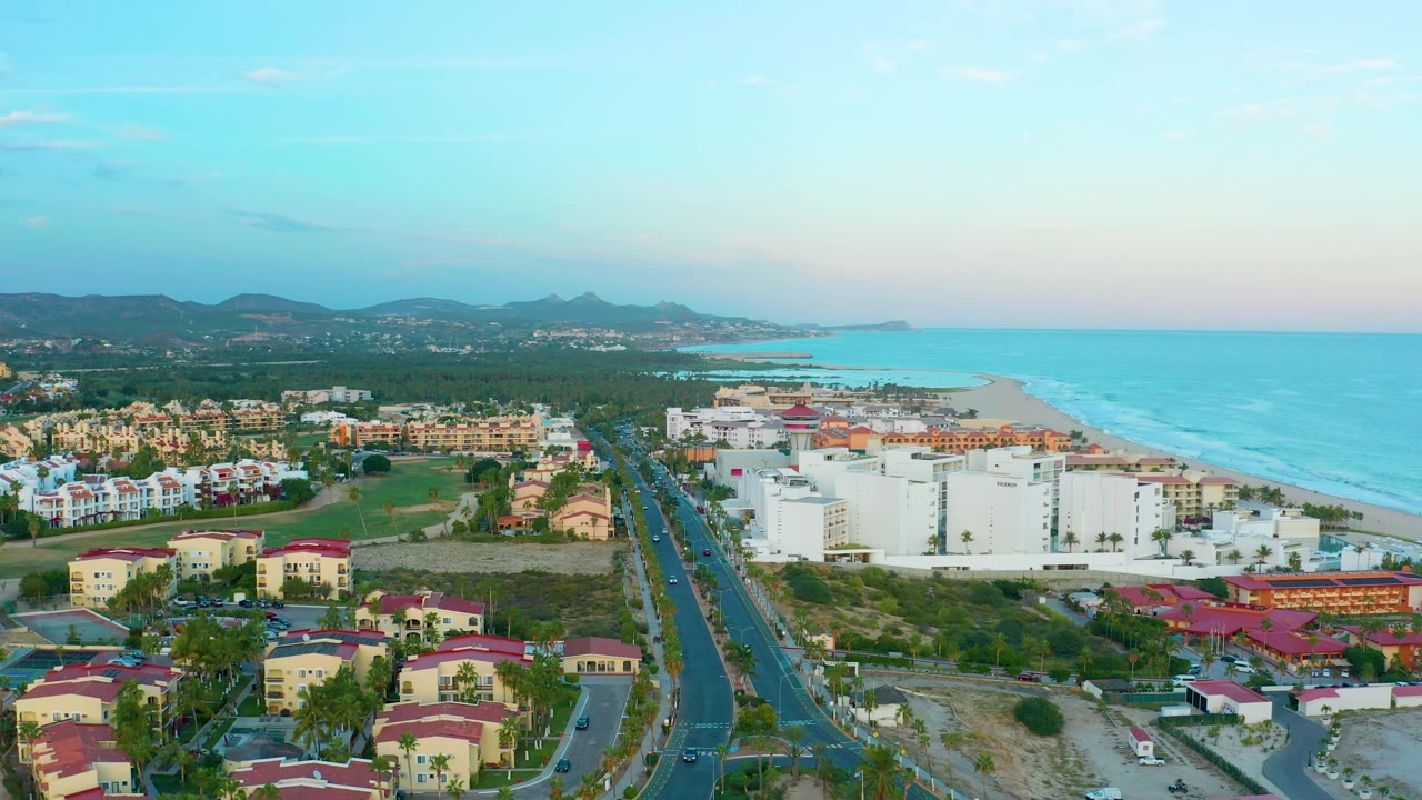 Aerial coastline view with road, homes, white buildings, beach, and ocean.