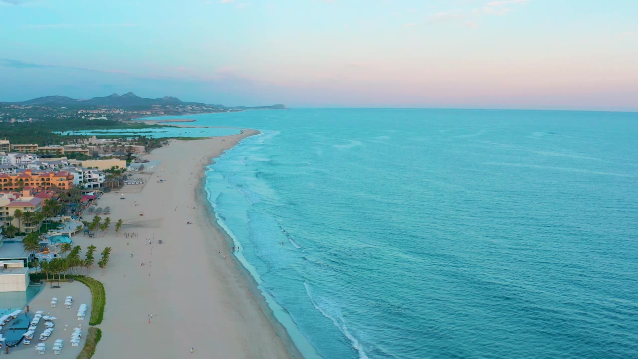 Drone view along the beach with resort-area buildings and ocean.