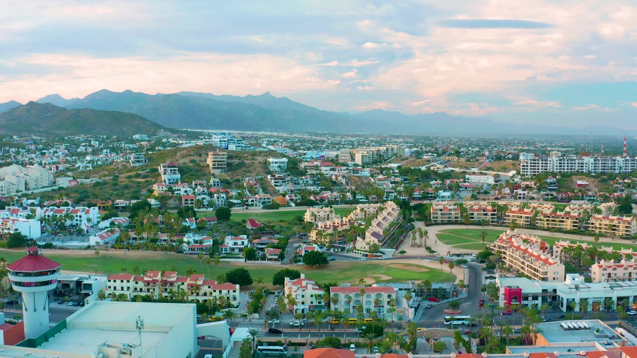 Aerial panorama of San Jose del Cabo with roads, residential buildings, green field, and hazy mountains.