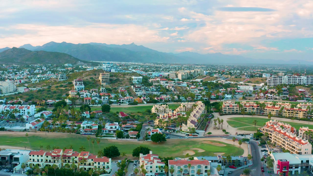 Aerial neighborhood view with curving road, grass, homes, and mountains.