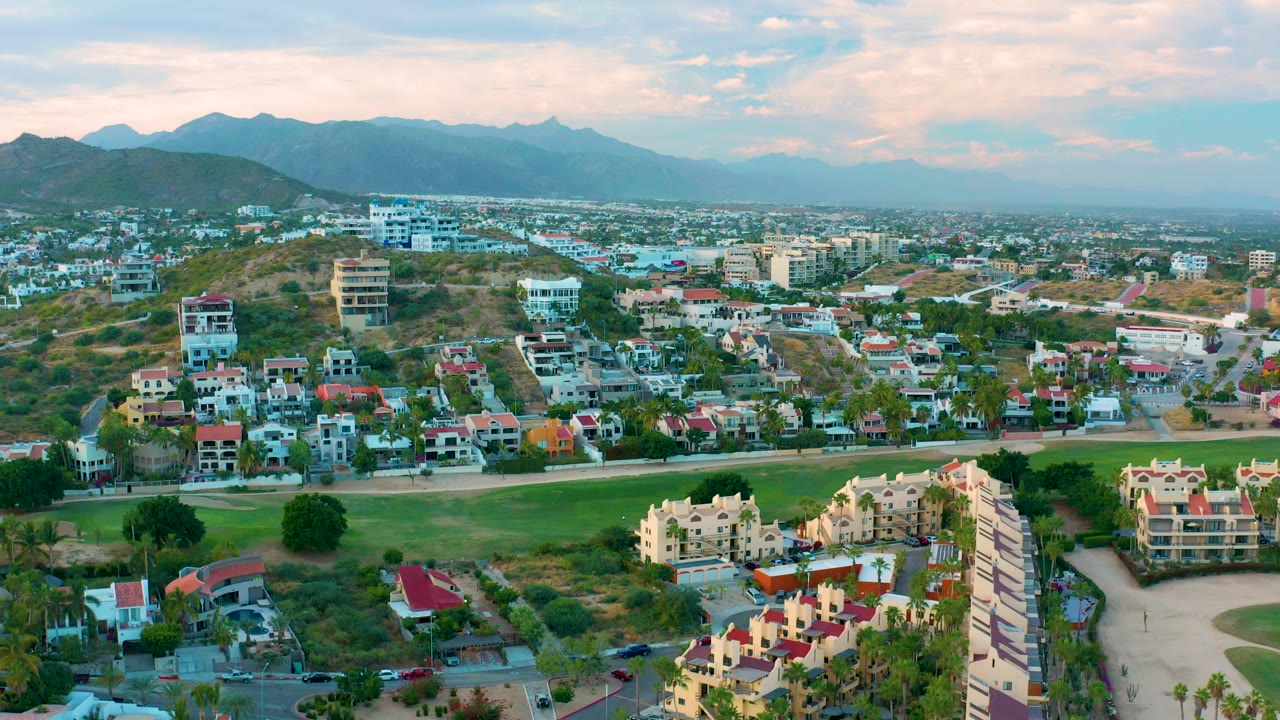 Hillside residential area with road, vegetation, and mountains beyond.