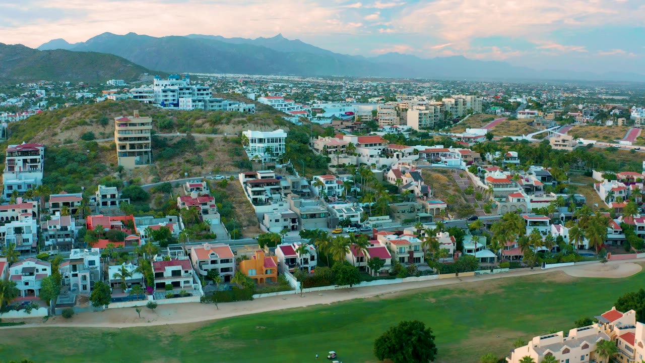Aerial neighborhood view with villas, hillside roads, and mountains.