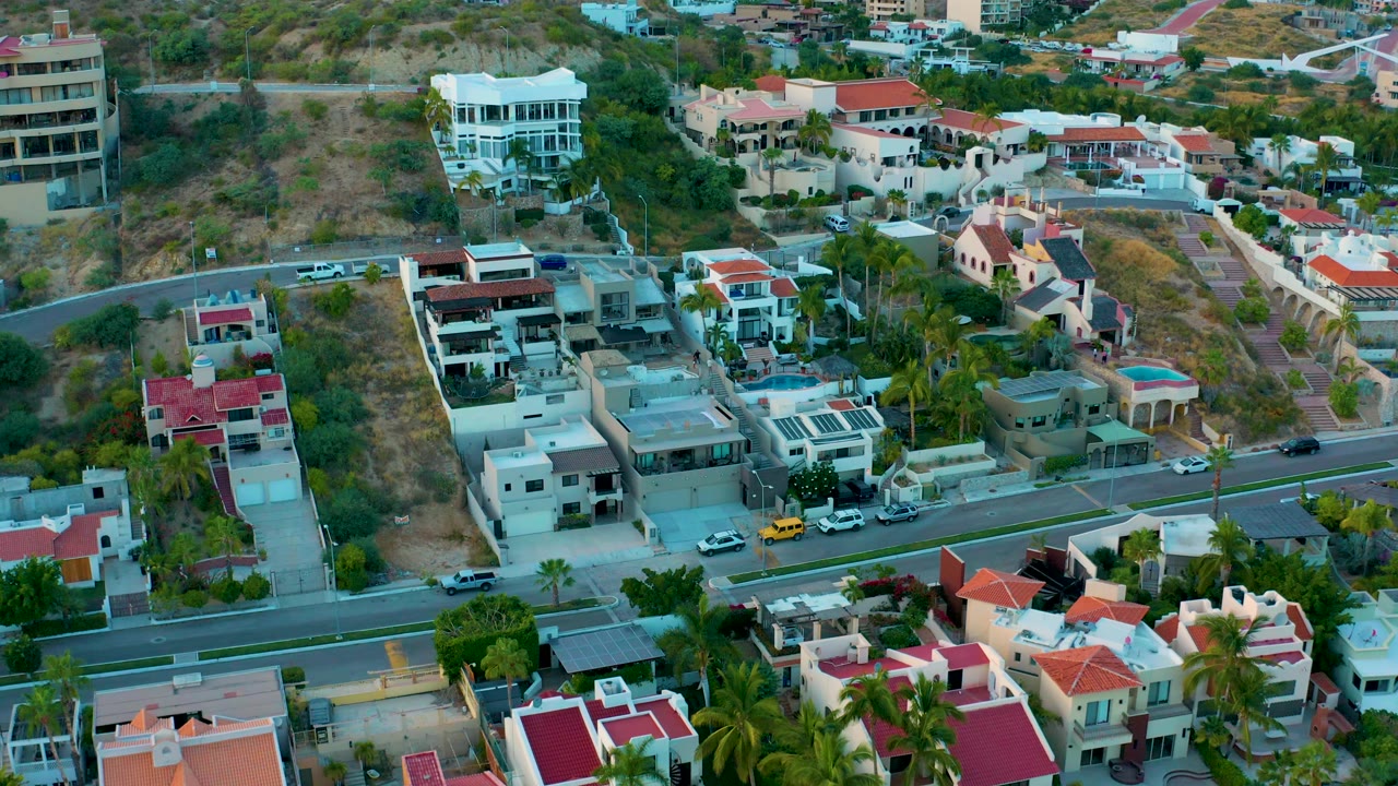 Aerial view of modern homes, a road, palms, and dry terrain.