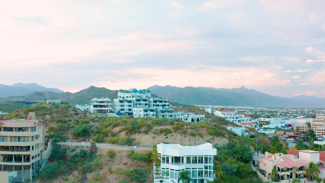 Residential hillside with white buildings, a road, city blocks, and mountains.